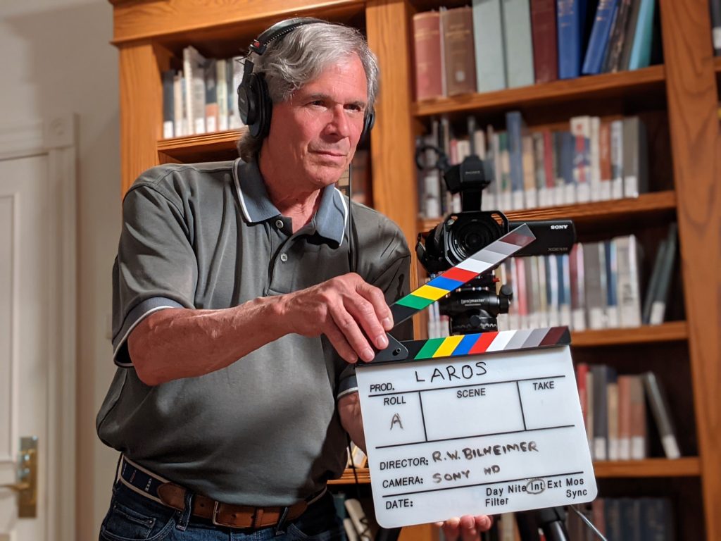 A man holds a clapboard in front of a camera